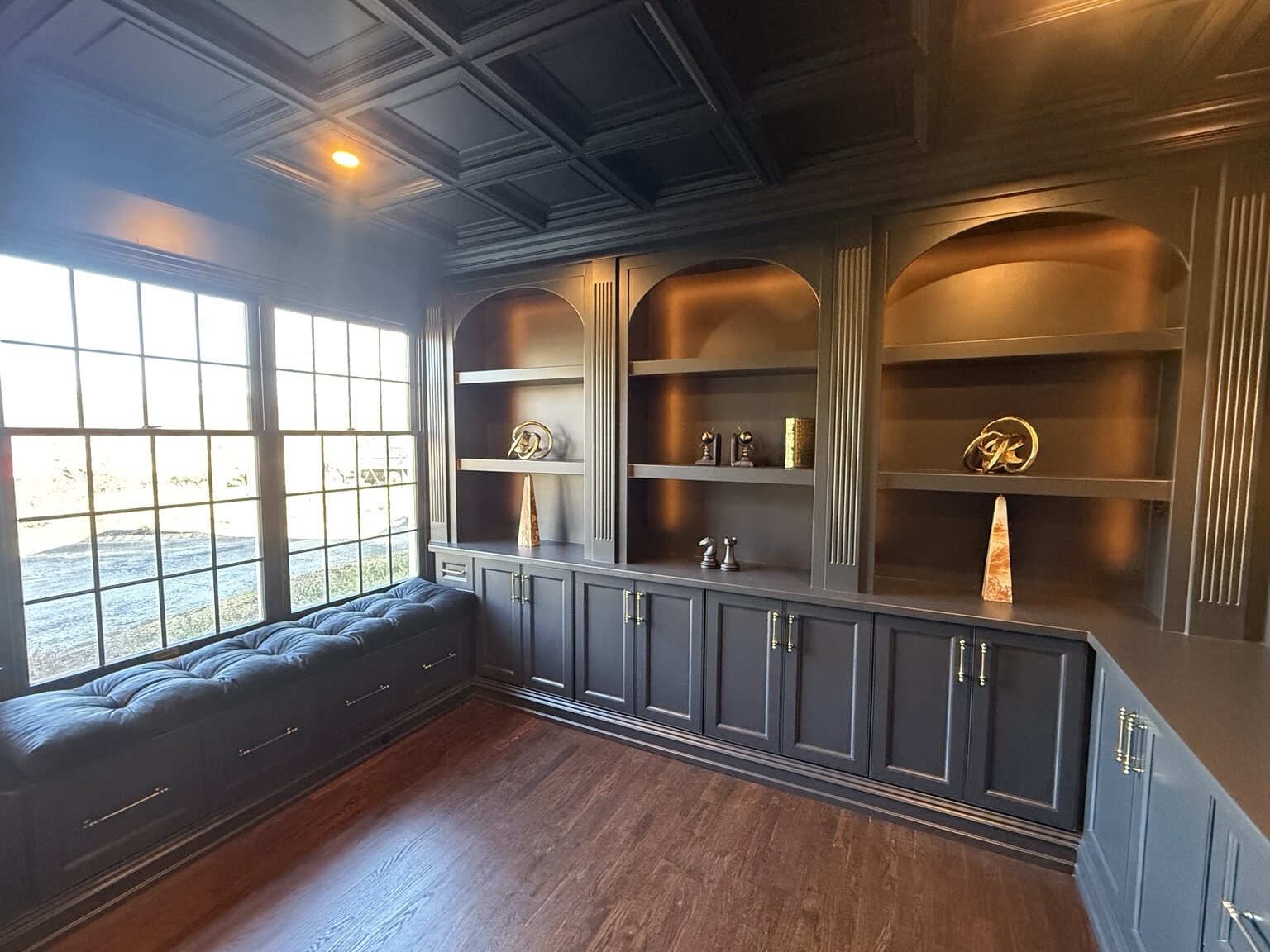 Dark painted library with arched built-in shelving and a window seat