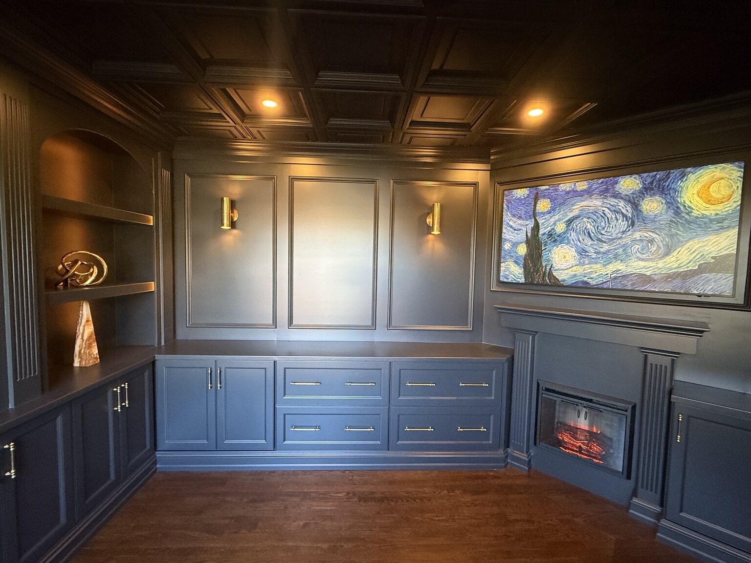 Dark painted library with paneled walls, built-in cabinetry, fireplace, and coffered ceiling