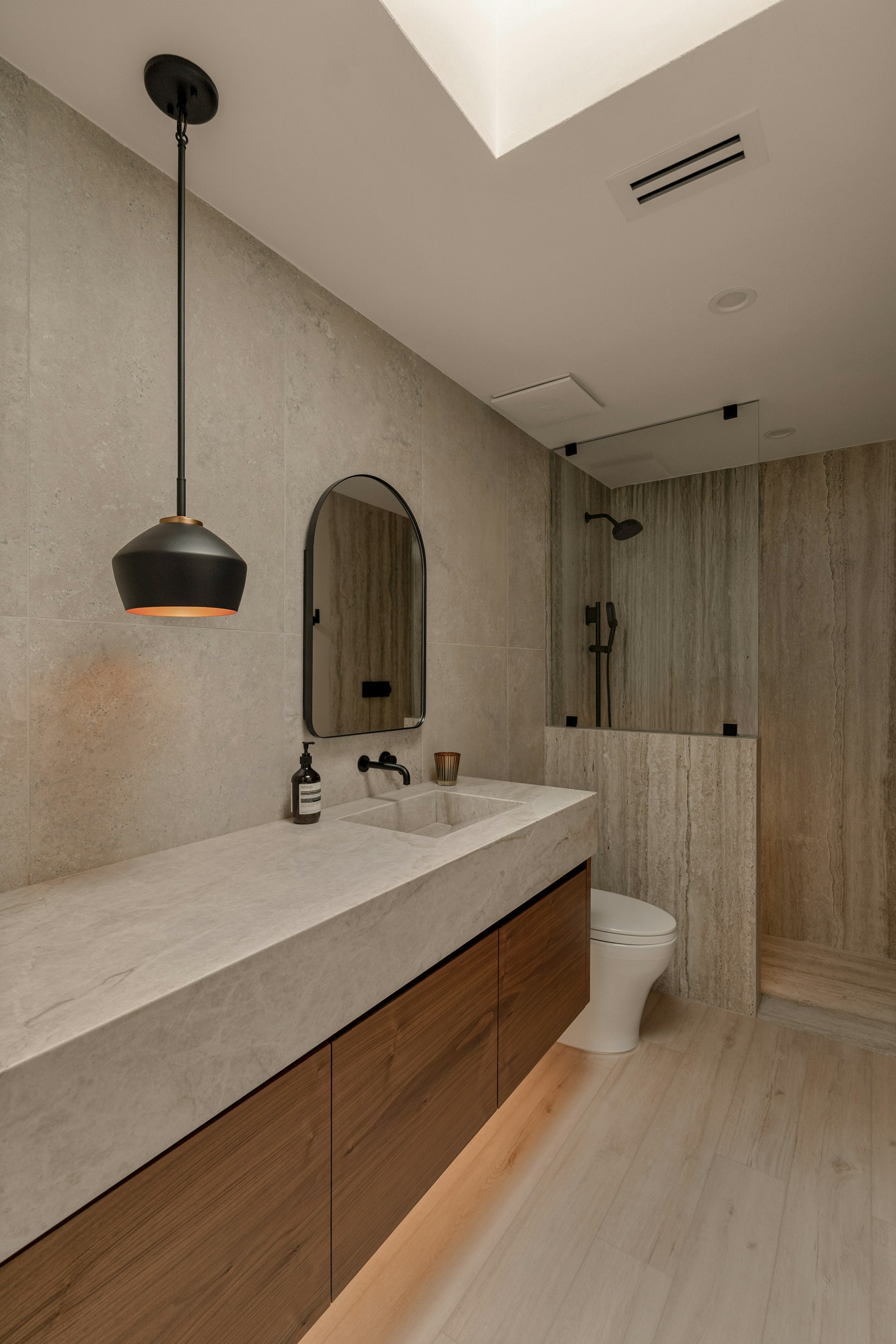 Warm wood bathroom vanity with a pale stone countertop in a refined modern bathroom